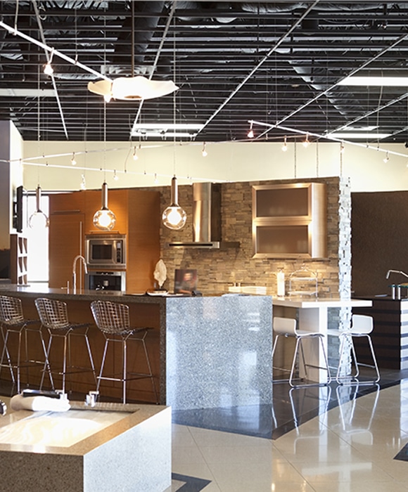 Showroom Cuisine Moderne : Design et Aménagement Haut de Gamme Showroom de cuisine moderne avec îlot en granit, tabourets en métal, meubles en bois et luminaires suspendus design.