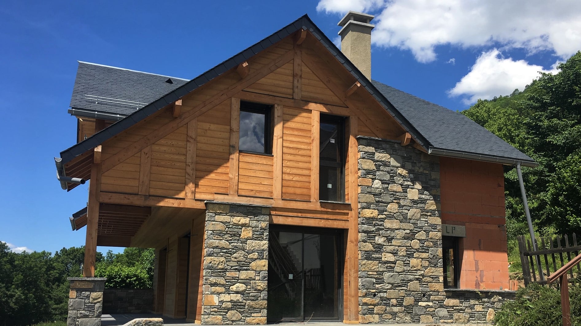 Construction de maison moderne en bois et pierre Maison contemporaine en bois et pierre en cours de construction avec toiture en ardoise et grandes fenêtres.