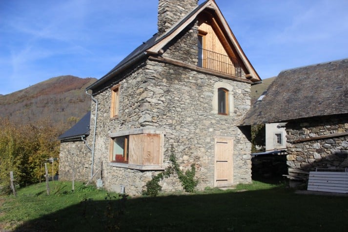 Maison en pierre authentique avec vue sur la montagne Maison traditionnelle en pierre et bois avec toit en ardoise dans un paysage de montagne ensoleillé.