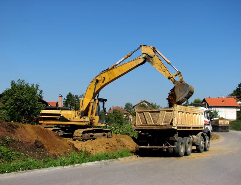 Pelleteuse chargeant de la terre dans un camion-benne Une pelleteuse jaune chargeant de la terre dans un camion-benne sur un chantier routier sous un ciel bleu dégagé.