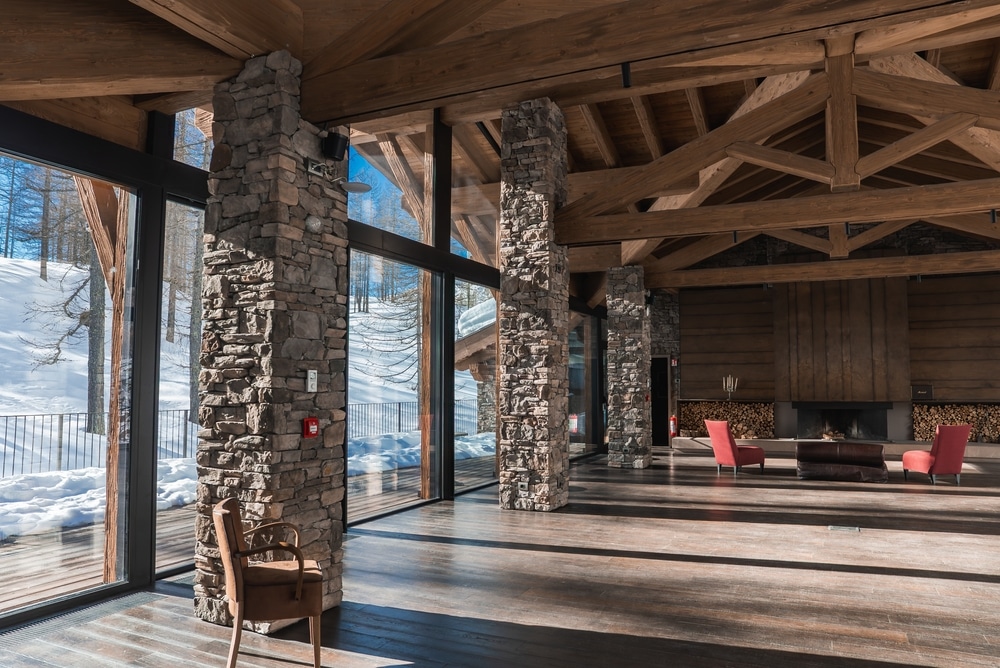 Salon de luxe avec vue sur la neige | Chalet de montagne Salon de chalet moderne avec colonnes en pierre, poutres apparentes et vue panoramique sur la neige.