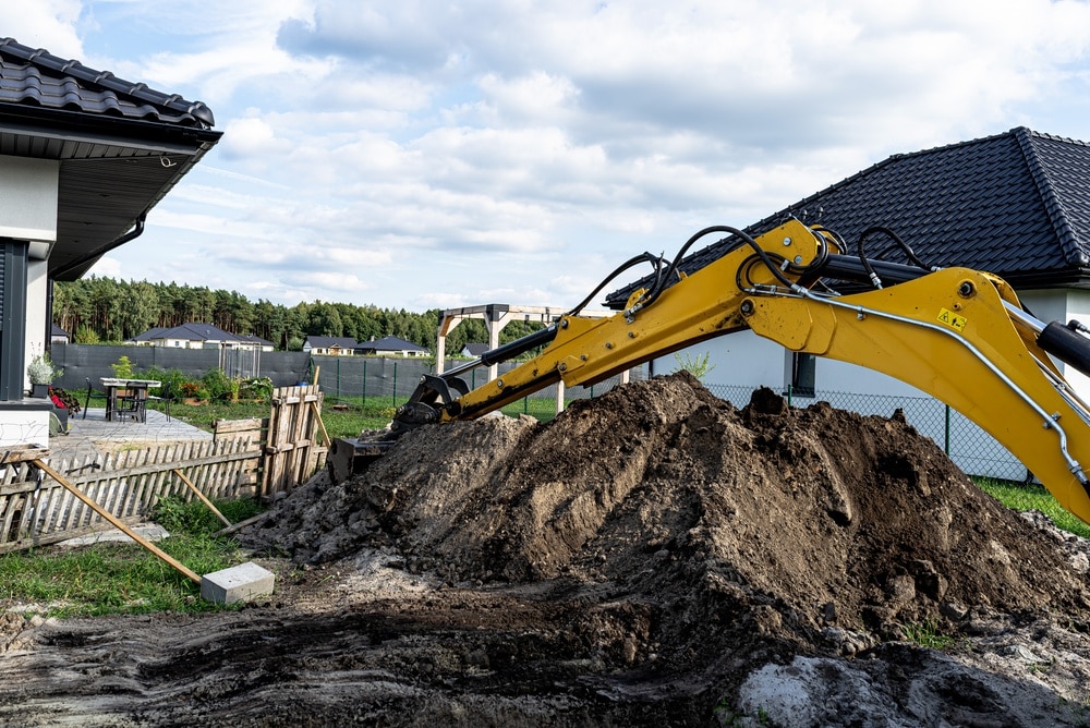 Terrassement de jardin résidentiel avec pelleteuse jaune Bras de pelleteuse jaune déplaçant de la terre pour un terrassement dans un jardin résidentiel.
